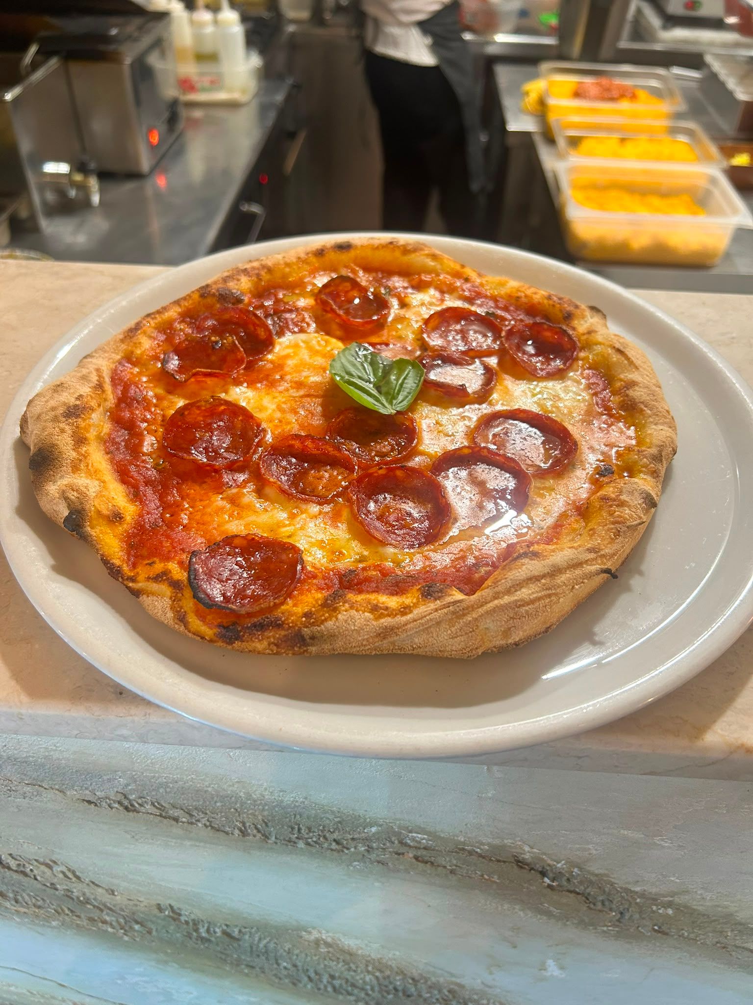 Pizza Diavola con salame piccante e una foglia di basilico, su piatto bianco sul banco di marmo