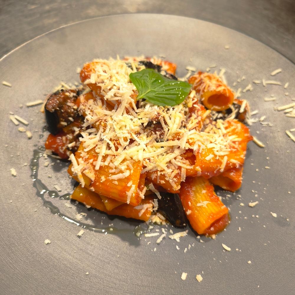 Rigatoni alla Norma con ricotta salata e una foglia di basilico, su piatto grigio